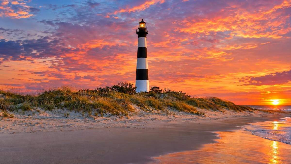 A striped lighthouse behind the dunes on North Carolina's Outer Banks at sunset